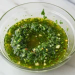 Vue de dessus d’un bol de chimichurri maison zoomé, avec persil, ail et piment.