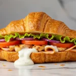 Croissant kebab garni de viande grillée, crudités fraîches et sauce blanche débordante sur fond marbré