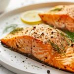Pavés de saumon au four dorés, servis avec citron et aneth sur un plan de travail en marbre blanc, lumière douce, cuisine moderne.
