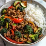 Sauté de viande hachée épicée avec légumes à l'ail et riz vapeur servi dans une assiette.